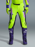 Pantalones Alpinestars Supertech Vista 2026, pantalones de motocross, amarillo fluorescente, morado y negro, usados con guantes a juego y botas moradas, con logotipos grandes degradados en los muslos, zonas perforadas para ventilación y un diseño atlético profesional para carreras todoterreno