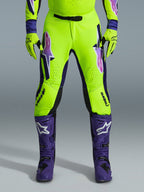 Pantalones Alpinestars Supertech Vista 2026, pantalones de motocross, amarillo fluorescente, morado y negro, usados con guantes a juego y botas moradas, con logotipos grandes degradados en los muslos, zonas perforadas para ventilación y un diseño atlético profesional para carreras todoterreno