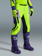 Alpinestars Supertech Vista Pants 2026, pantalones de motocross, amarillo neón brillante, morado y negro, combinados con botas moradas y guantes amarillos a juego, con logotipos llamativos en el muslo y un ajuste atlético de alto rendimiento