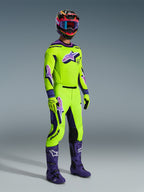 Pantalones Alpinestars Supertech Vista 2026, pantalones de motocross, amarillo neón y púrpura, usados con jersey de carreras a juego, botas púrpuras y casco colorido, con paneles de cuero negro en las rodillas, logotipos Astar llamativos en púrpura y zonas de ventilación perforadas, conjunto coordinado para carreras off-road.