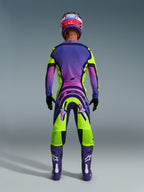 Alpinestars Supertech Vista Pants 2026, pantalones de motocross, amarillos, morados y negros, vista trasera de un piloto de motocross con un conjunto completo de equipación de carreras con un jersey de degradado morado y botas moradas, diseño atlético vibrante para competición profesional off-road