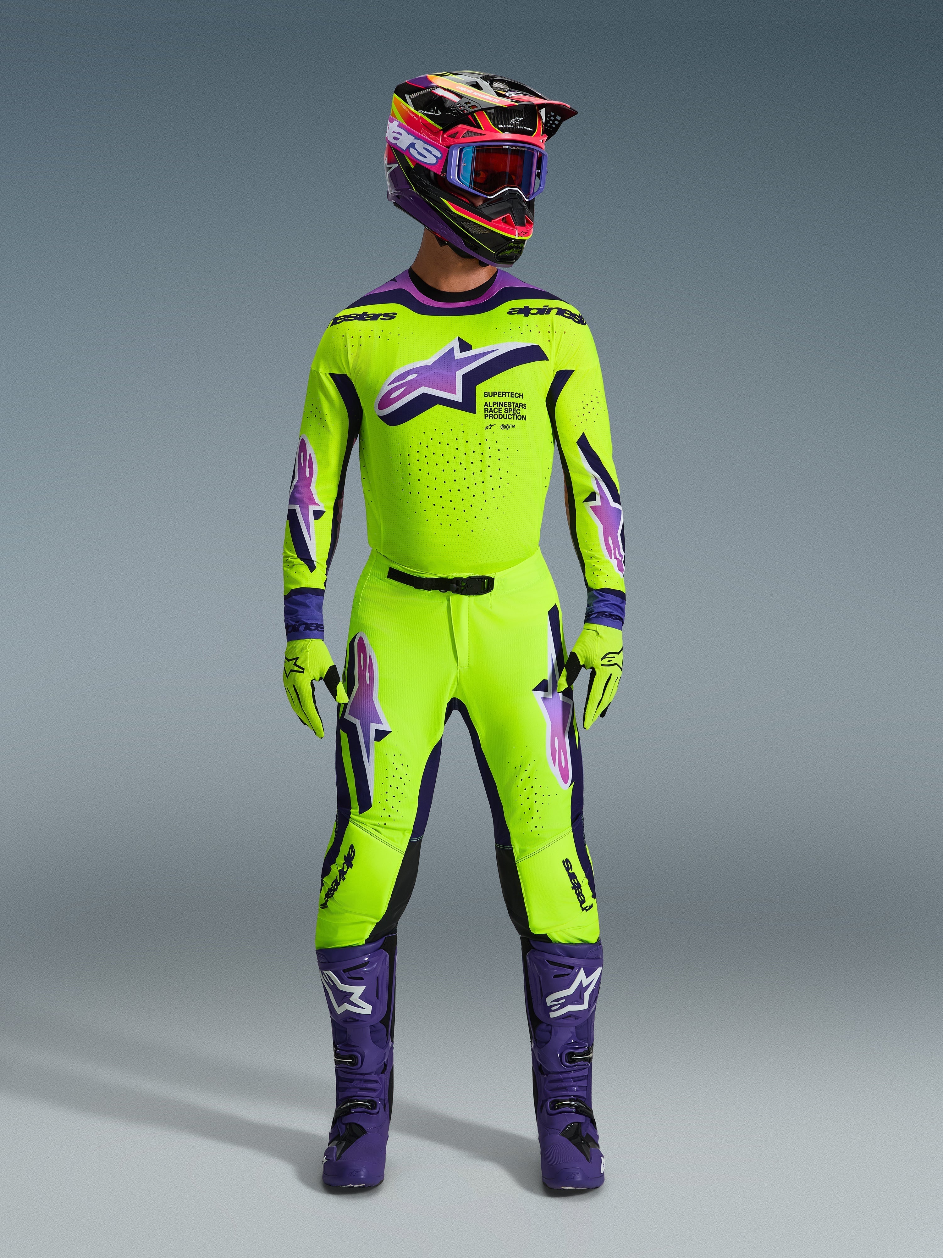 Motocross rider wearing the Alpinestars 2026 Supertech Vista Jersey in bright yellow with purple and black accents, matching yellow and purple pants, purple boots, and coordinated helmet and gloves, complete professional racing gear set