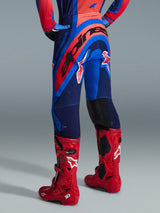 Alpinestars 2026 Supertech Vista Pants, pantalones de motocross, azul marino oscuro, Hot Coral y cobalto, vista trasera del piloto, combinados con botas de motocross rojas, marca llamativa en la parte trasera, ajuste atlético con zonas elásticas y construcción rip-stop duradera para competición profesional