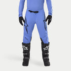 Pantalones Alpinestars Supertech Dade 2024, pantalones de motocross, azul claro, con grandes logotipos Astars negros en los muslos y hebilla negra en la cintura, combinados con botas de motocross negras y prenda superior azul a juego, equipamiento profesional para carreras todoterreno