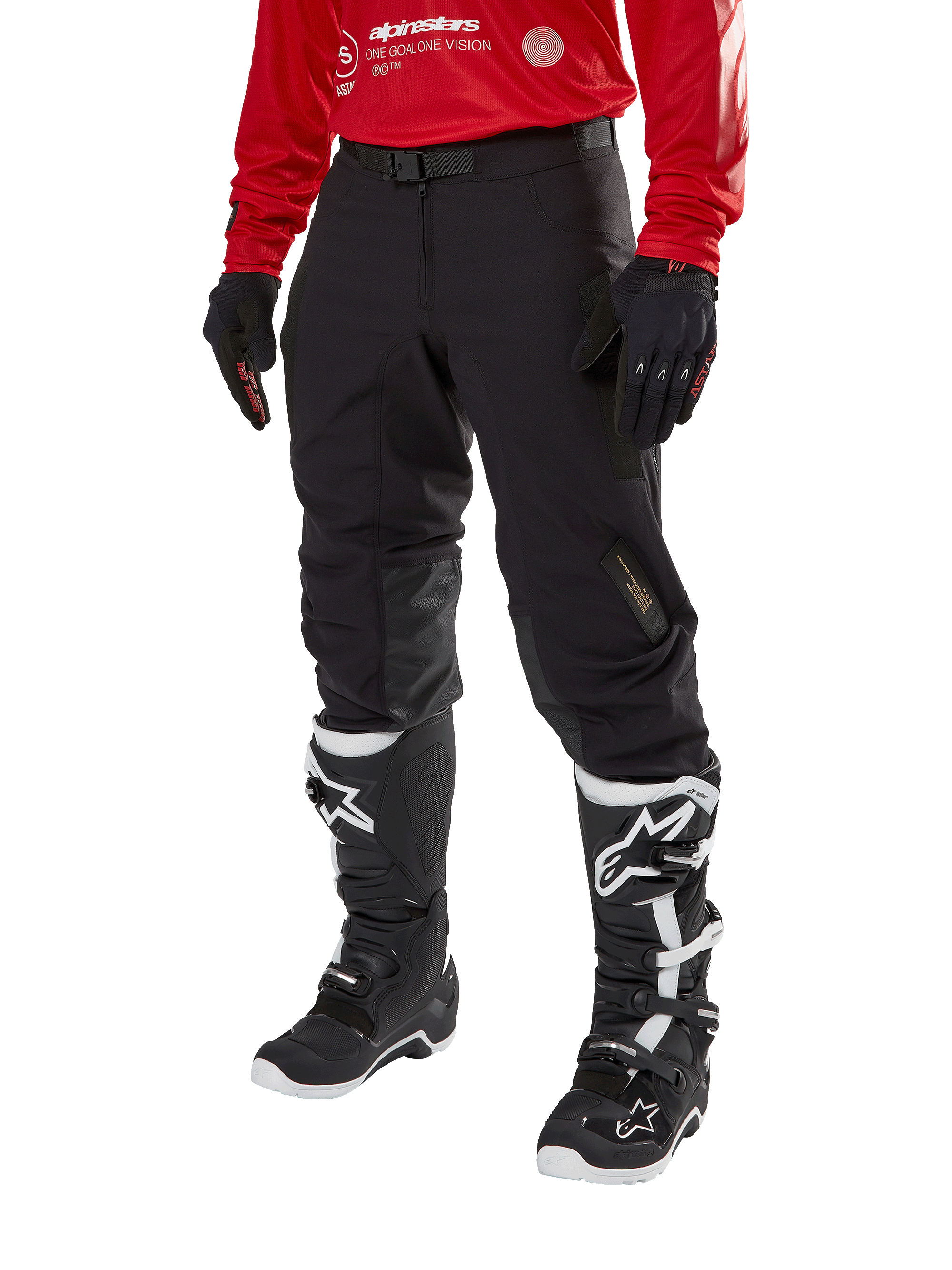 Alpinestars Techdura Pants, pantalones de moto todoterreno negros, combinados con un jersey rojo de manga larga y botas de motocross negras y blancas, con construcción de poliamida elástica resistente, refuerzos de cuero en el interior de las rodillas y cinturón ajustable con hebilla para enduro