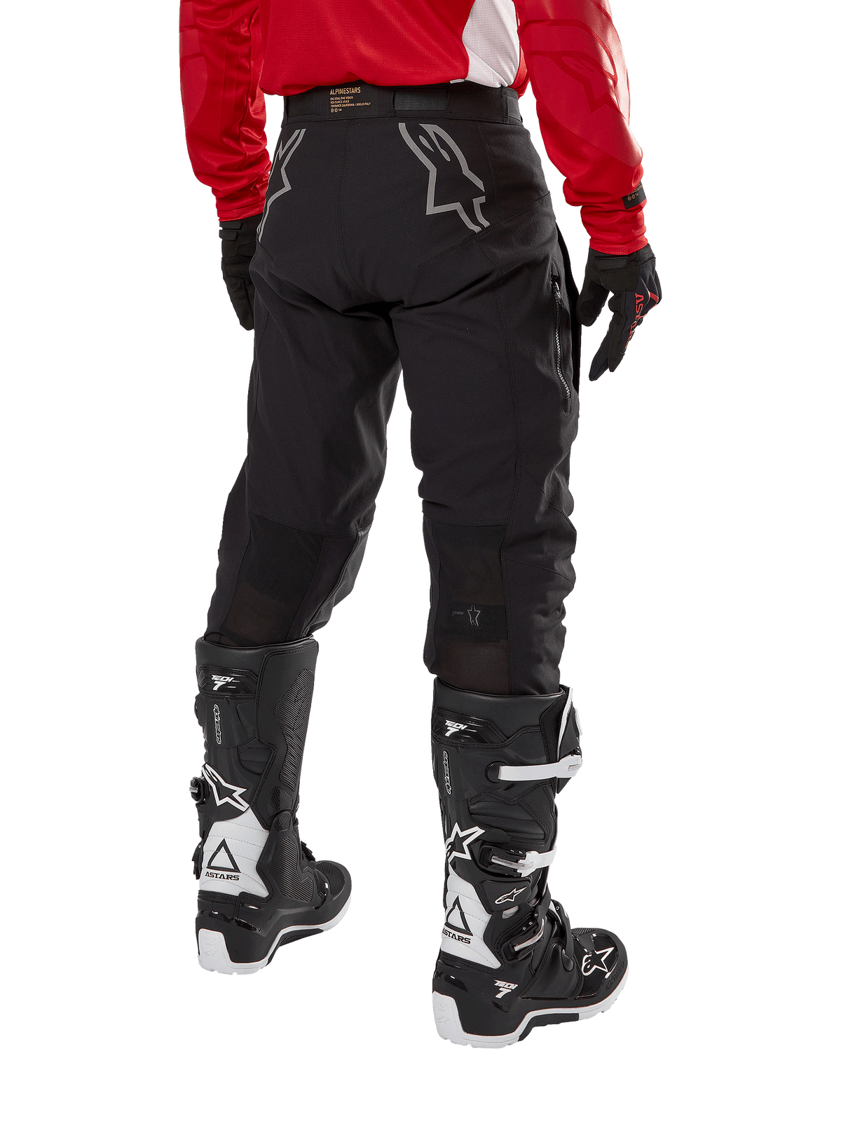 Alpinestars Techdura Pants, pantalones de enduro off-road, negros, vista posterior que muestra logotipos de estrellas grises en el asiento, usados con jersey rojo de manga larga y botas Tech 7 en blanco y negro, construcción textil resistente para conducción de aventura.