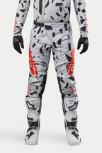 Pantalones Alpinestars Techstar Rantera 2024, pantalones de motocross, Haze Gray Camo, usados con jersey a juego, guantes negros y botas blancas, con un patrón de manchas negras y logotipo de Alpinestars en rojo, diseño duradero para carreras off-road