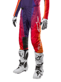 Alpinestars 2024 Techstar Pneuma Pants, pantalones de motocross para hombre con diseño en degradado de púrpura, naranja y azul, logo blanco de Alpinestars, material técnico para alto rendimiento, combinados con botas de motocross blancas y guantes blancos