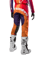 Alpinestars 2024 Techstar Pneuma Pants, pantalones de motocross para hombre, colores morado, naranja y azul profundo, vista trasera con logo blanco, combinados con botas blancas y guantes negros, material técnico y duradero para off-road