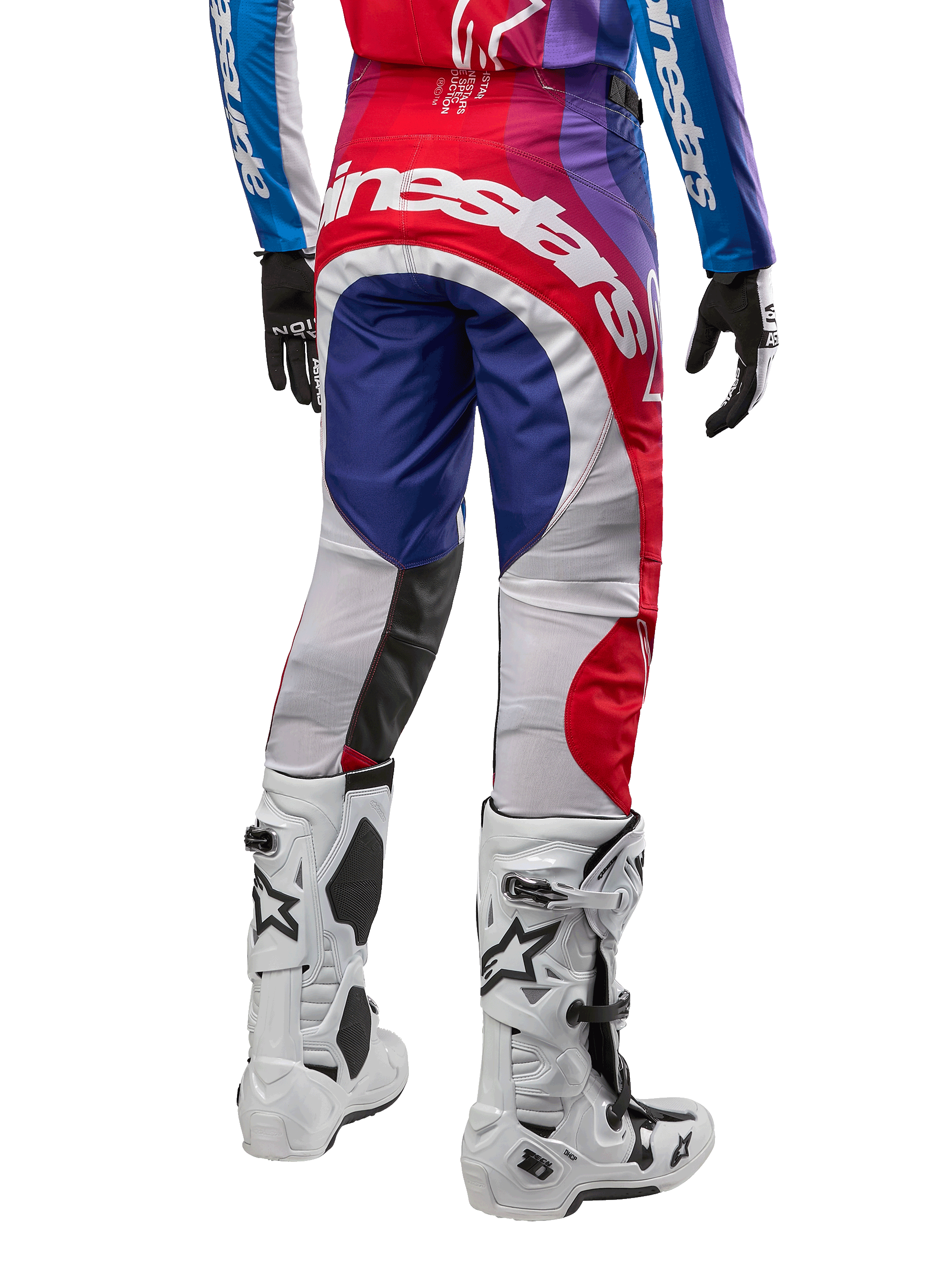 Alpinestars Pantalones Techstar Pneuma 2024, pantalones de motocross, Blu Mars Red White, vista trasera usados con jersey a juego y botas blancas, con logotipo blanco llamativo en el asiento y paneles multicolores, equipamiento profesional de motocross