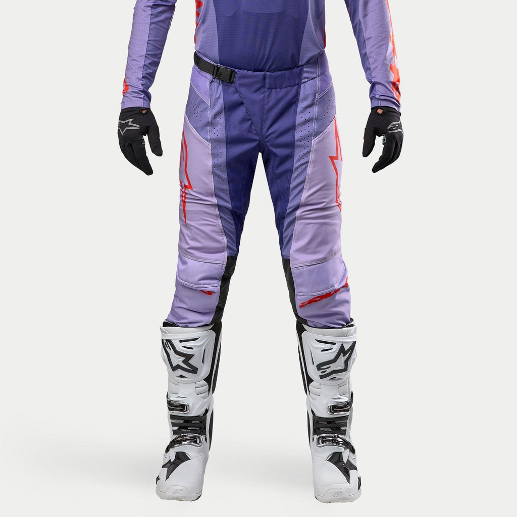 Alpinestars Techstar Ocuri Pants 2024, pantalones de motocross para hombre en color púrpura y naranja intenso, diseño deportivo con logotipos rojos, combinados con guantes negros y botas de motocross blancas y negras, equipamiento de alto rendimiento para off-road.