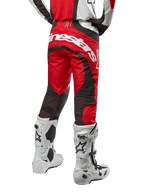 Pantalones Alpinestars Techstar Ocuri 2024, pantalones de motocross, rojo Marte, blanco y negro, vista trasera con un gran logotipo blanco de Alpinestars en la zona del asiento, paneles de ventilación de malla negra, combinados con botas de motocross blancas y negras, diseño de ajuste atlético de competición para conducción todoterreno