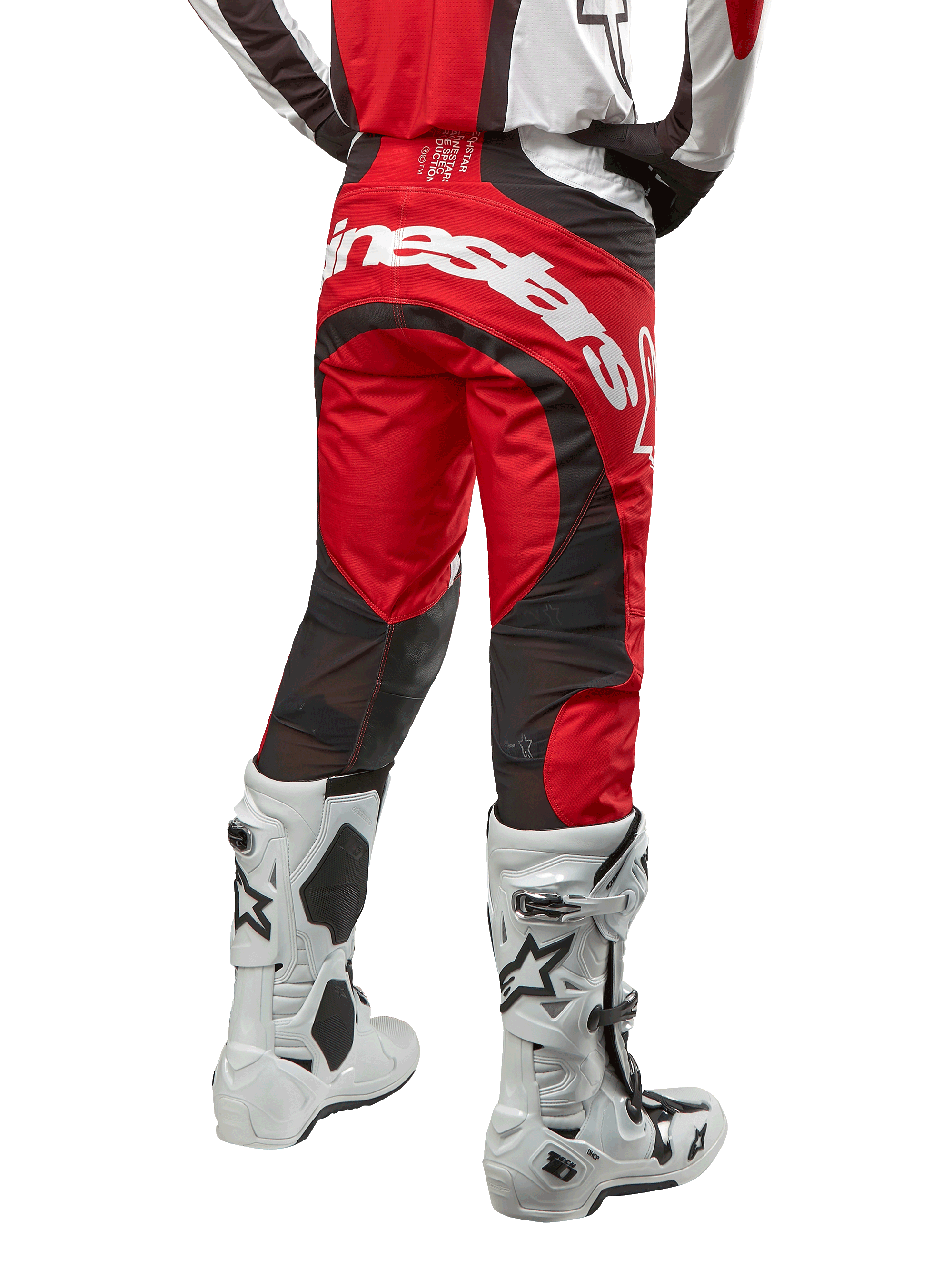 Pantalones Alpinestars Techstar Ocuri 2024, pantalones de motocross, rojo Marte, blanco y negro, vista trasera con un gran logotipo blanco de Alpinestars en la zona del asiento, paneles de ventilación de malla negra, combinados con botas de motocross blancas y negras, diseño de ajuste atlético de competición para conducción todoterreno