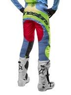 Alpinestars Techstar Ocuri Pants 2024, pantalones de motocross, azul claro, amarillo flúor y rojo, vista trasera con botas de motocross blancas y negras, con un diseño vibrante de bloques de color y el logotipo de Alpinestars en el asiento.