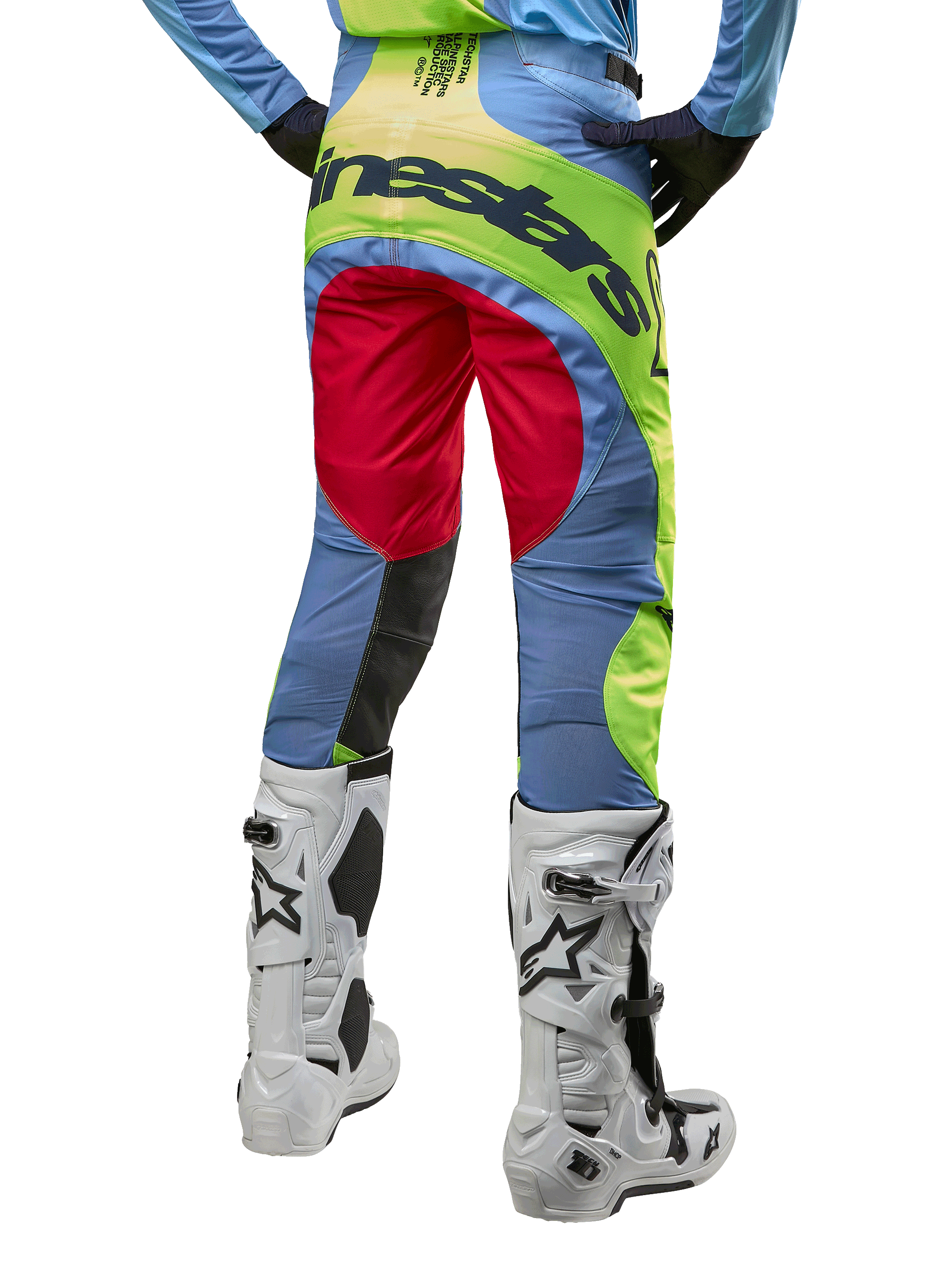 Alpinestars Techstar Ocuri Pants 2024, pantalones de motocross, azul claro, amarillo flúor y rojo, vista trasera con botas de motocross blancas y negras, con un diseño vibrante de bloques de color y el logotipo de Alpinestars en el asiento.