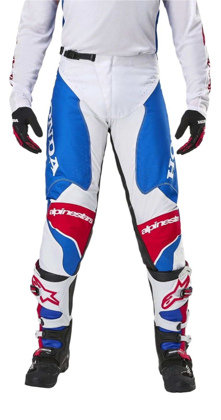 Alpinestars Honda Racer Iconic Pants, pantalones de motocross, blanco, azul brillante y rojo brillante, vista frontal mostrada en un piloto con equipamiento a juego, con logotipos de Honda grandes en los laterales y paneles rojos en las rodillas con la marca Alpinestars, ajuste atlético para carreras fuera de carretera