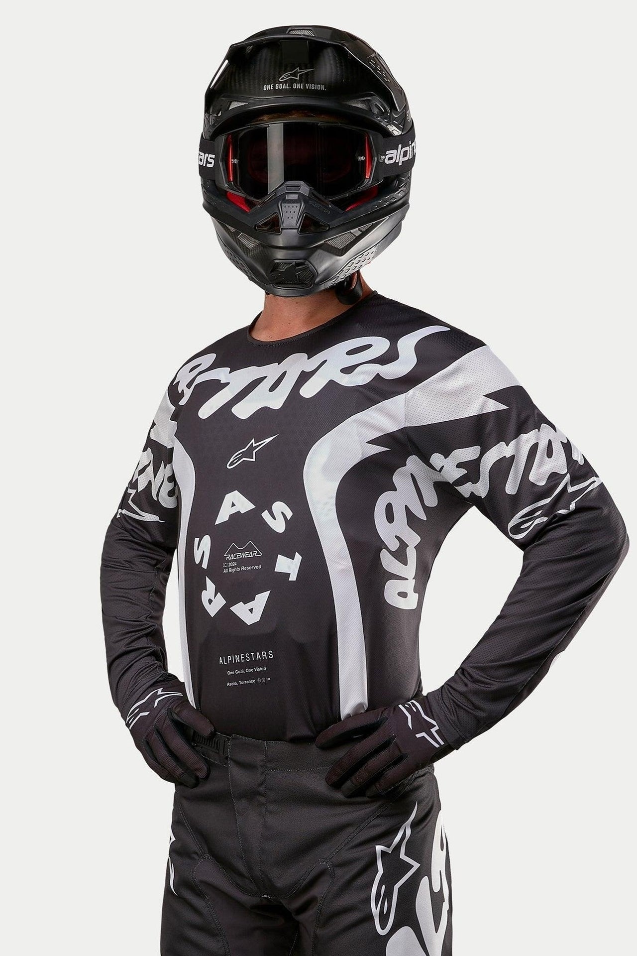 Alpinestars 2024 Racer Hana Jersey, jersey de motocross, negro y blanco, con llamativos gráficos de texto y logo de Alpinestars en blanco, usado por un piloto con casco y gafas negros, equipamiento de alto rendimiento para carreras todoterreno