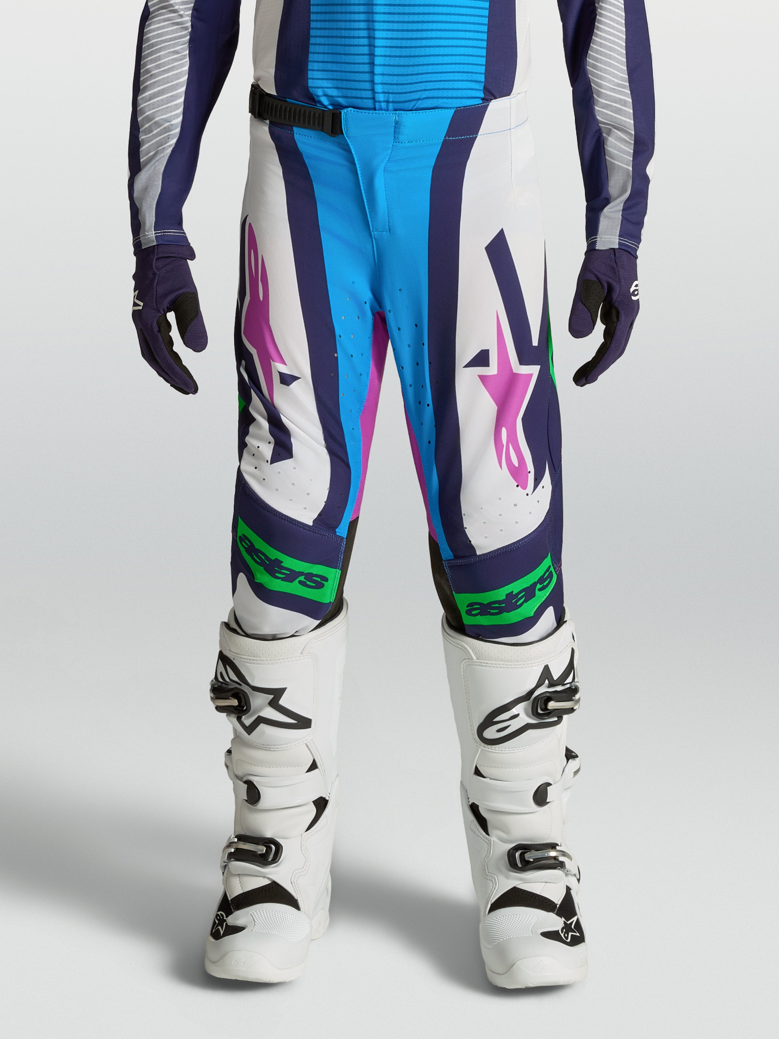 Alpinestars Pantalones Supertech Maven Juvenil, equipo de motocross blanco y azul con detalles verde flúor y rosa.