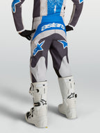 Pantalones Fluid Drag Juvenil, pantalones de motocross para niños en gris y azul, vista trasera en piloto con botas blancas, equipo técnico para conducción off-road