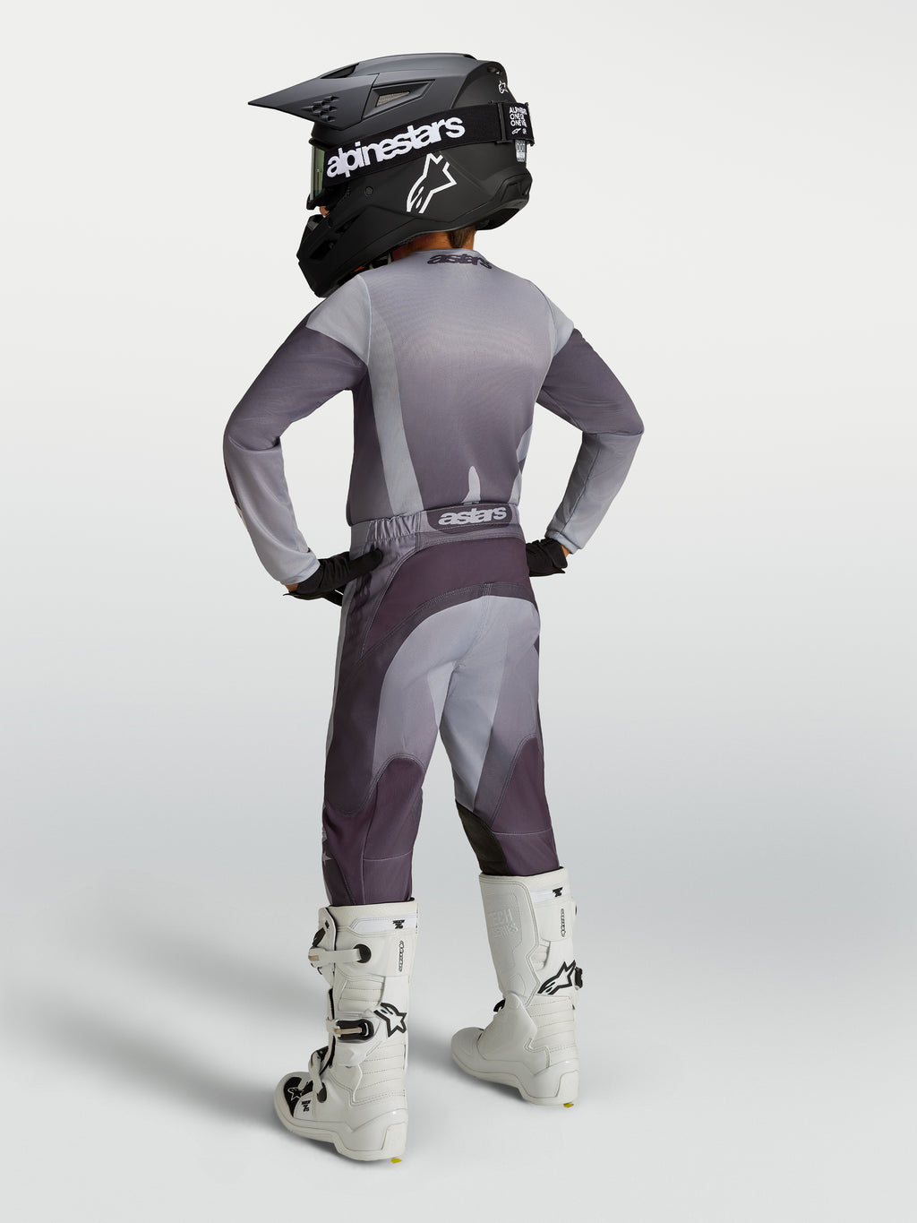 Alpinestars Pantalones Fluid Amber Juvenil, equipo de motocross gris y morado carbón, ajuste deportivo, con botas blancas.