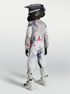 Alpinestars Pantalones Fluid Lone Juvenil, equipo de motocross gris camuflaje y blanco con detalles rojos, diseño para off-road en un piloto juvenil visto desde atrás.