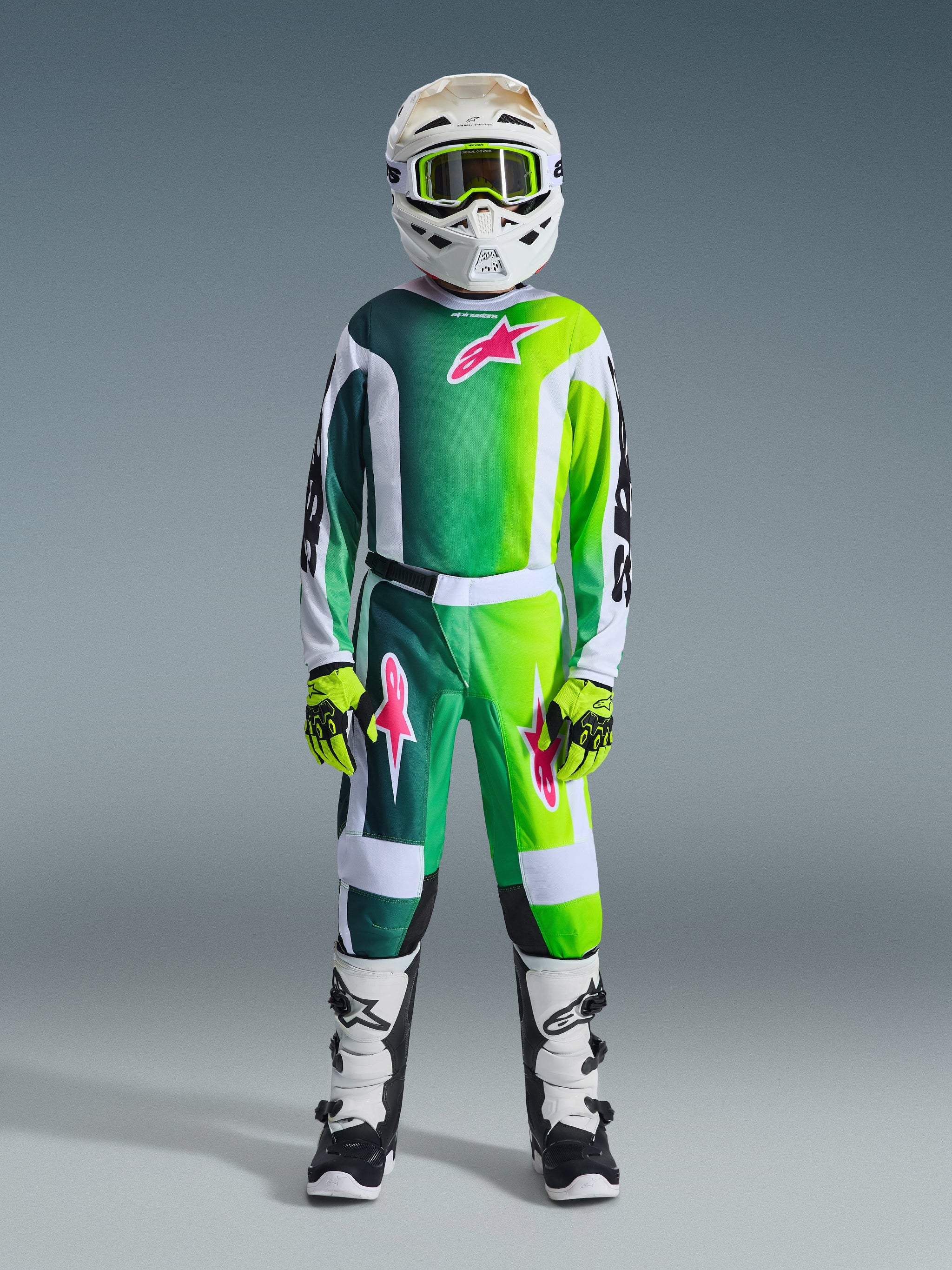 Alpinestars 2026 Youth Fluid Portl Pants, Motocross Pants, Green White and Black, worn by a youth rider in full racing gear including a matching gradient jersey, white helmet with lime goggles, and black and white boots, featuring pink star logos and a durable sport-fit design.