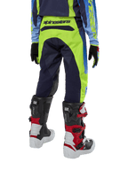 Pantalones Alpinestars Youth 2024 Racer Hoen, pantalones de motocross, amarillo flúor y azul noche, vista trasera con marca Alpinestars destacada en la cintura, usados con botas Tech Series negras y rojas y jersey a juego, diseño deportivo duradero para conducción off-road juvenil