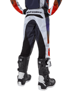 Alpinestars 2024 Youth Racer Hoen Pants, pantalones de motocross juveniles, gris claro con detalles en naranja intenso y negro, vista trasera con paneles negros en el asiento y las piernas, marca destacada en la parte trasera de la cintura, combinados con botas de motocross blancas y negras para carreras todoterreno