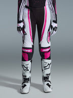 Alpinestars 2026 Stella Techstar Nomur para mujer, pantalones de motocross, negro, blanco y fucsia, usados con jersey de carreras, guantes a juego y botas de motocross blancas, con gráficos rosas llamativos y logotipos astars en las rodillas, diseñados para competición off-road de alto nivel.