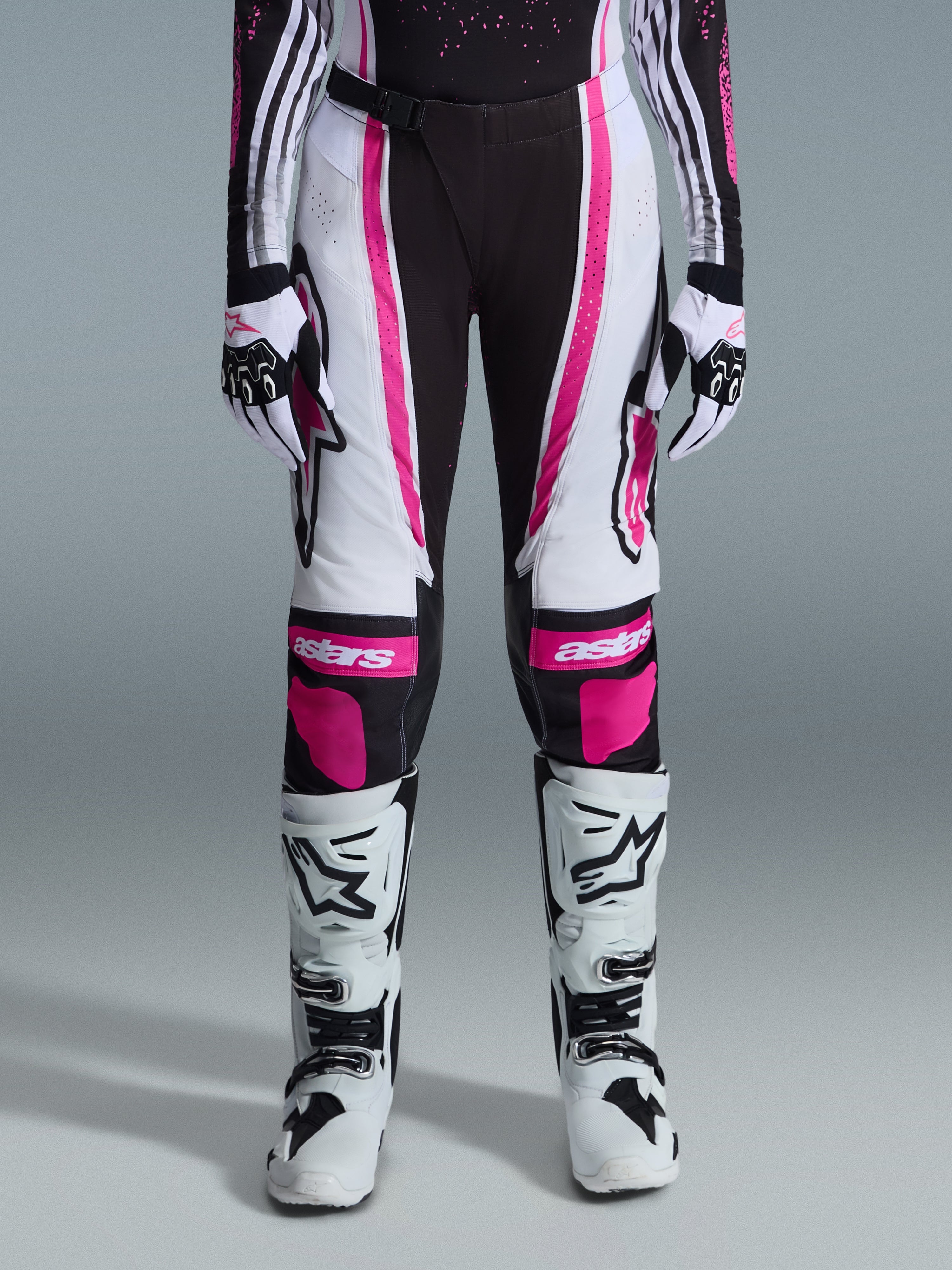 Alpinestars 2026 Stella Techstar Nomur para mujer, pantalones de motocross, negro, blanco y fucsia, usados con jersey de carreras, guantes a juego y botas de motocross blancas, con gráficos rosas llamativos y logotipos astars en las rodillas, diseñados para competición off-road de alto nivel.