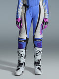Pantalones Alpinestars Stella Techstar Nomur 2026 para mujer, pantalones de motocross, azul claro, blanco roto y negro, combinados con botas de motocross blancas y guantes rosas y negros, con el logotipo 'astars' en las rodillas y un diseño técnico de múltiples paneles para pilotos femeninas.