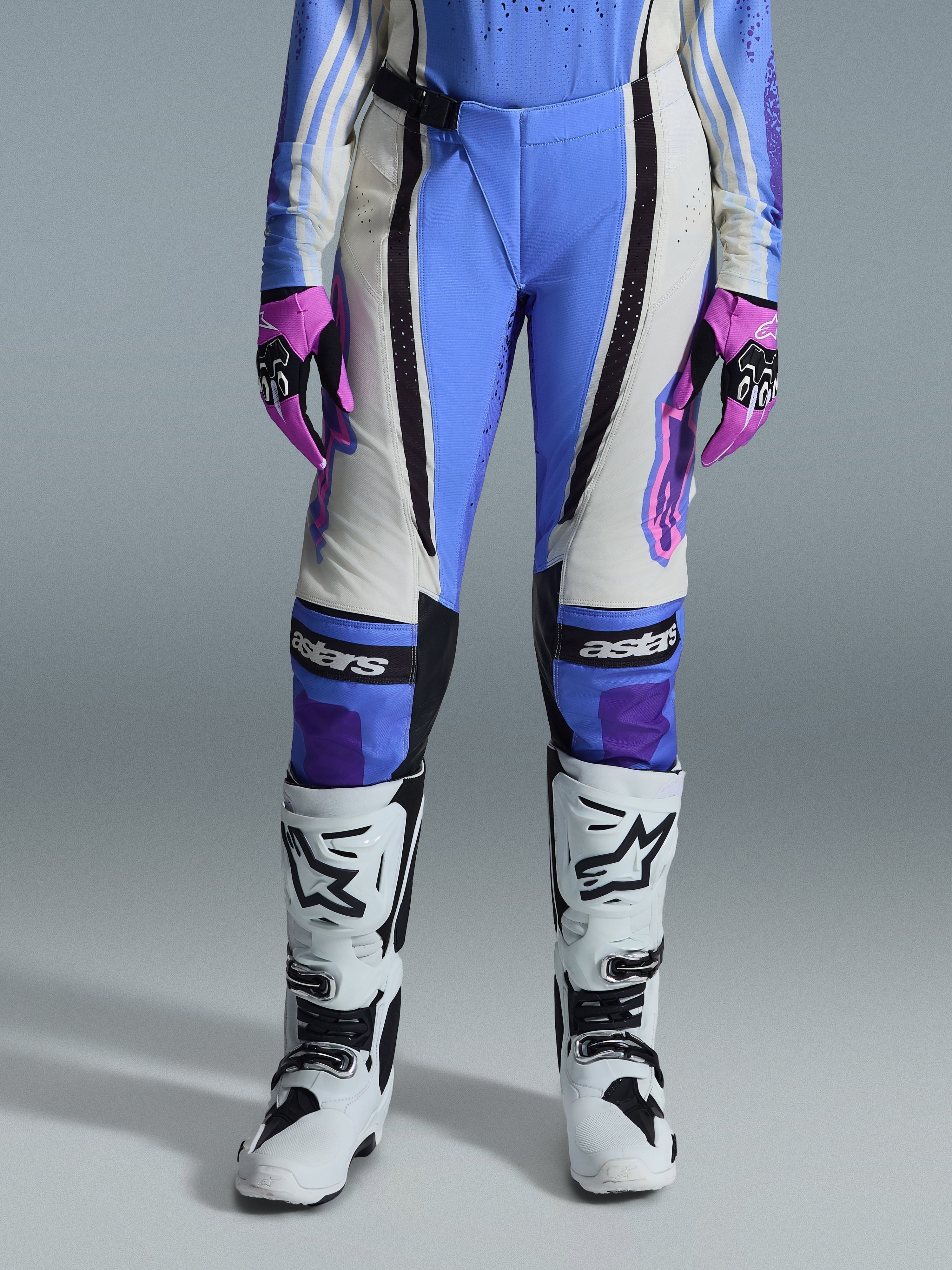 Pantalones Alpinestars Stella Techstar Nomur 2026 para mujer, pantalones de motocross, azul claro, blanco roto y negro, combinados con botas de motocross blancas y guantes rosas y negros, con el logotipo 'astars' en las rodillas y un diseño técnico de múltiples paneles para pilotos femeninas.