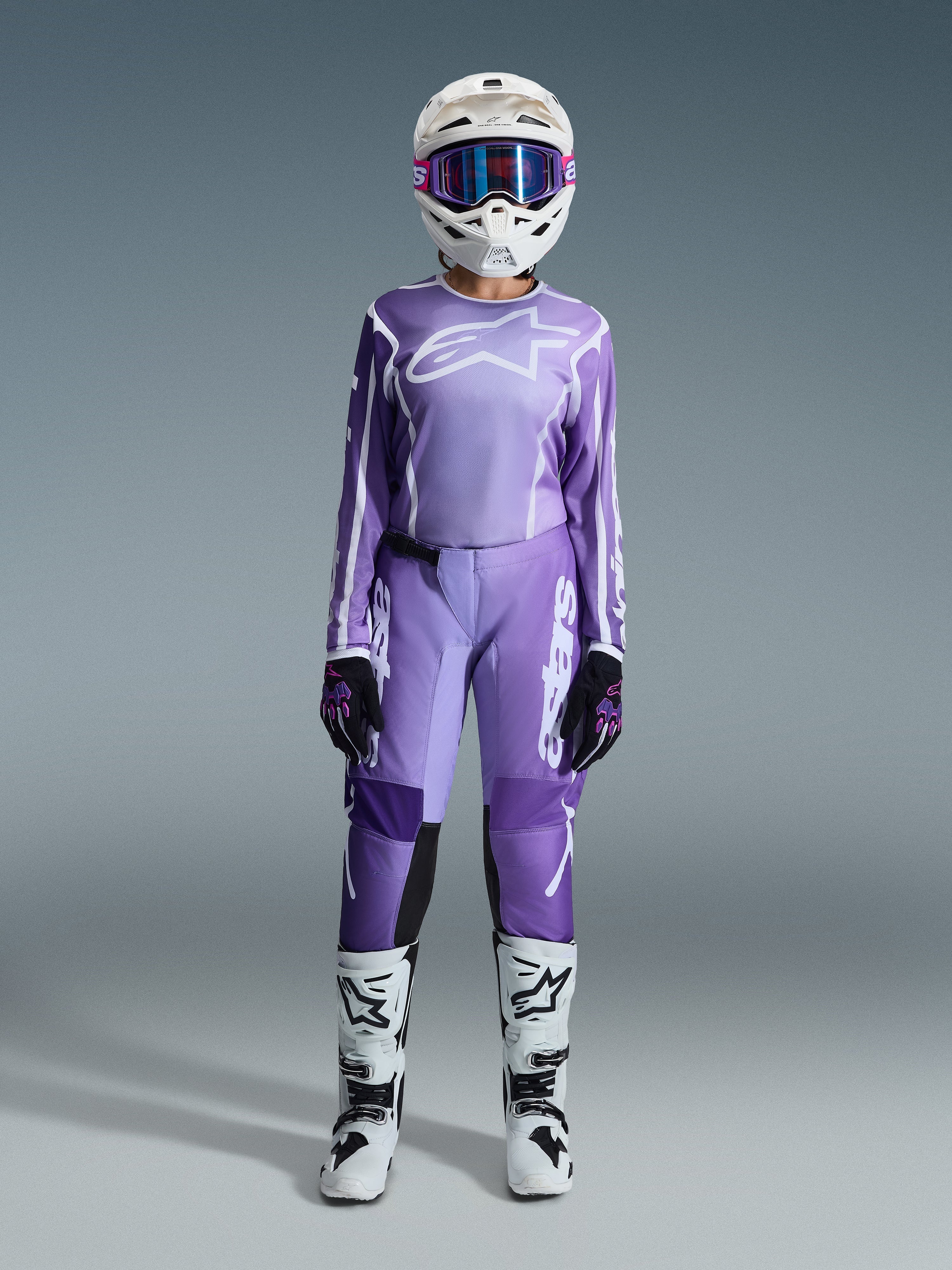 Alpinestars Stella Fluid Apex 2026 para mujer, piloto de motocross con jersey violeta y blanco, pantalones a juego, casco blanco con gafas rosas y botas de motocross blancas y negras, kit de competición completo para mujer