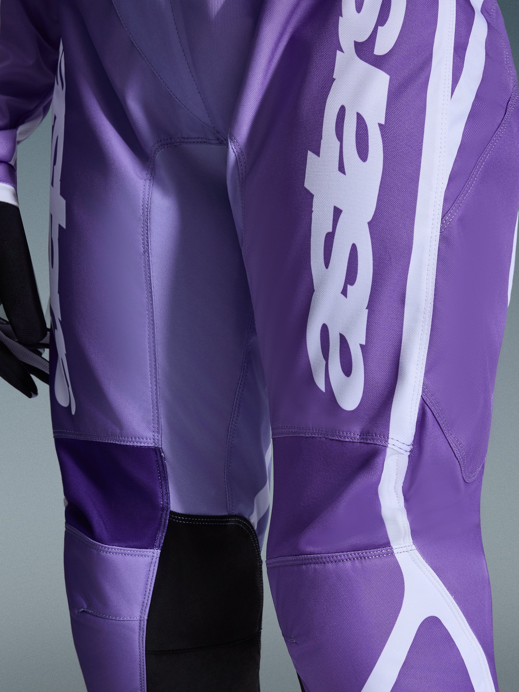 Alpinestars Stella Fluid Apex Pants 2026, pantalones de motocross para mujer, violeta y blanco, primer plano con el logotipo en blanco sobre tejido morado, paneles interiores de las rodillas reforzados en negro, construcción de polifabric duradera para conducción off-road