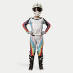Piloto de motocross con pantalones Alpinestars Stella Techstar para mujer 2024, Negro Multicolor con base blanca y franjas rojas, amarillas y azules, jersey de manga larga a juego, casco blanco y botas negras, equipo completo de carreras para competición todoterreno