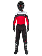 Piloto de motocross vistiendo el Jersey Alpinestars Pro-Dura en negro, rojo brillante y blanco, combinado con pantalones negros, botas negras y un casco negro, equipo completo de carreras off-road.