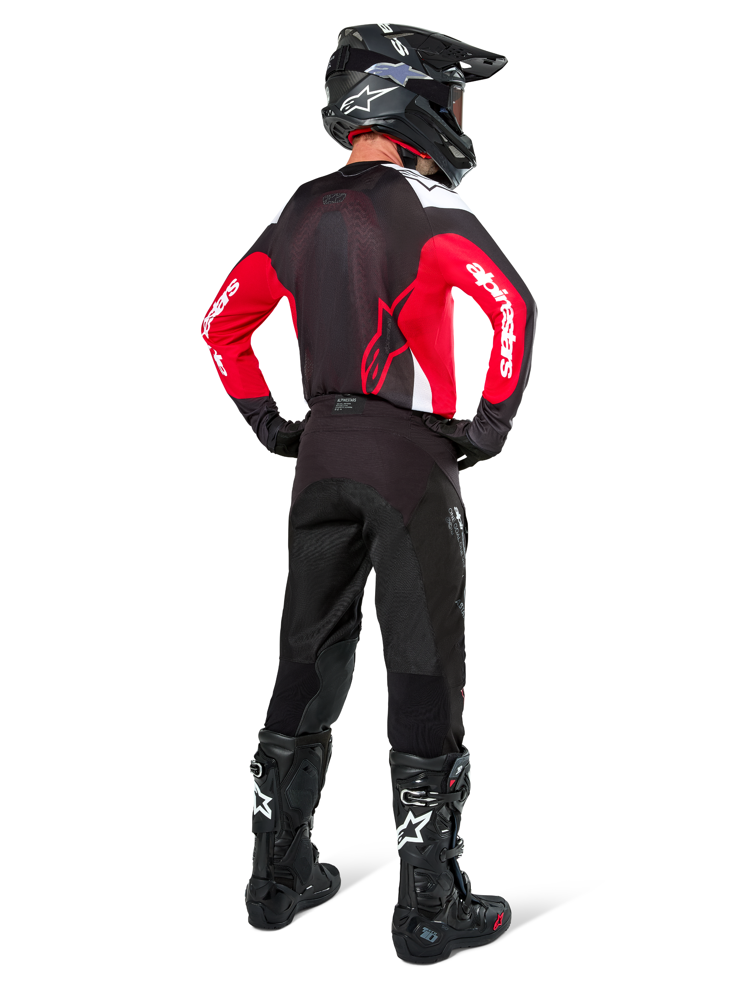 Piloto de motocross de espaldas con el Jersey Alpinestars Pro-Dura en negro, rojo brillante y blanco, combinado con pantalones, casco y botas de motocross negros, mostrando el diseño trasero y los logotipos en las mangas, equipamiento coordinado para carreras todoterreno.