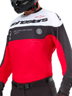 Jersey Alpinestars Pro-Dura, jersey de motocross y enduro, negro, rojo brillante y blanco, con gráfico 'ONE GOAL. ONE VISION.' y perforaciones láser en el pecho, usado con pantalones de motocross negros y casco.