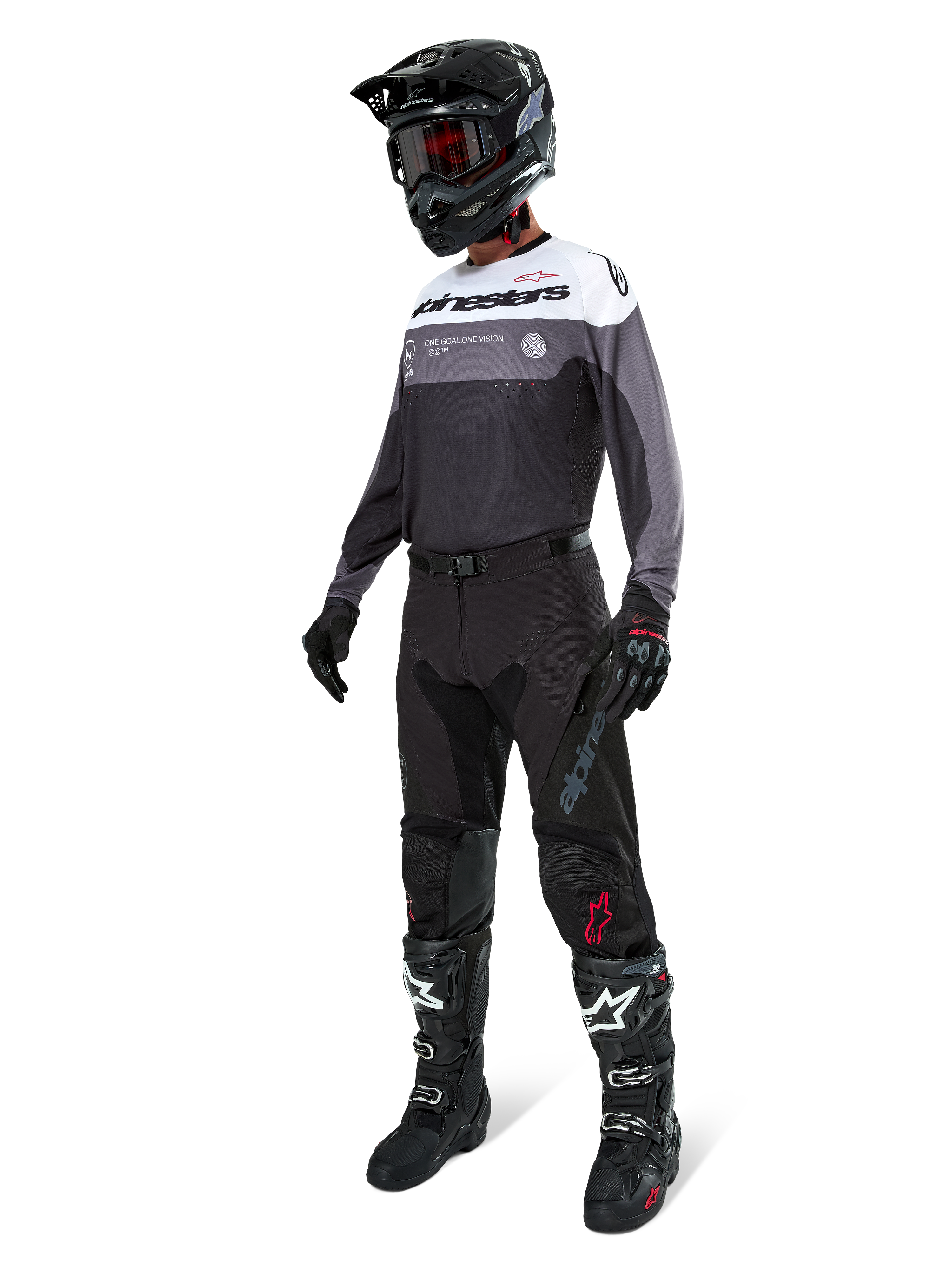 Jersey Alpinestars Pro-Dura en Black Magnet White, usado por un piloto de motocross con equipamiento completo que incluye pantalones negros, casco negro con gafas y botas blancas y negras. El jersey presenta un diseño técnico de bloques de color con paneles blancos, grises y negros, diseñado para el rendimiento en enduro y conducción off-road.
