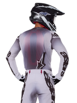 Motocross rider from behind wearing the Alpinestars 2025 Supertech Maker Jersey, Silver and Black with a red mesh back panel and black sleeve logos, paired with matching motocross pants and a black and white helmet, professional off-road racing gear