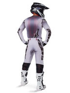 Alpinestars Supertech Maker Jersey 2025, jersey de motocross, plata y negro, vista trasera de un piloto con equipamiento a juego y botas blancas, con el distintivo logotipo de Alpinestars en las mangas y el logo de la estrella en la espalda, ajuste atlético de competición para un rendimiento profesional todoterreno.