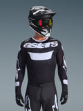 Alpinestars 2026 Racer Air Riway Jersey, jersey de motocross en blanco y negro con marca 'astars', usado por un piloto con casco, gafas y pantalones negros a juego, con paneles de malla transpirable para carreras todoterreno