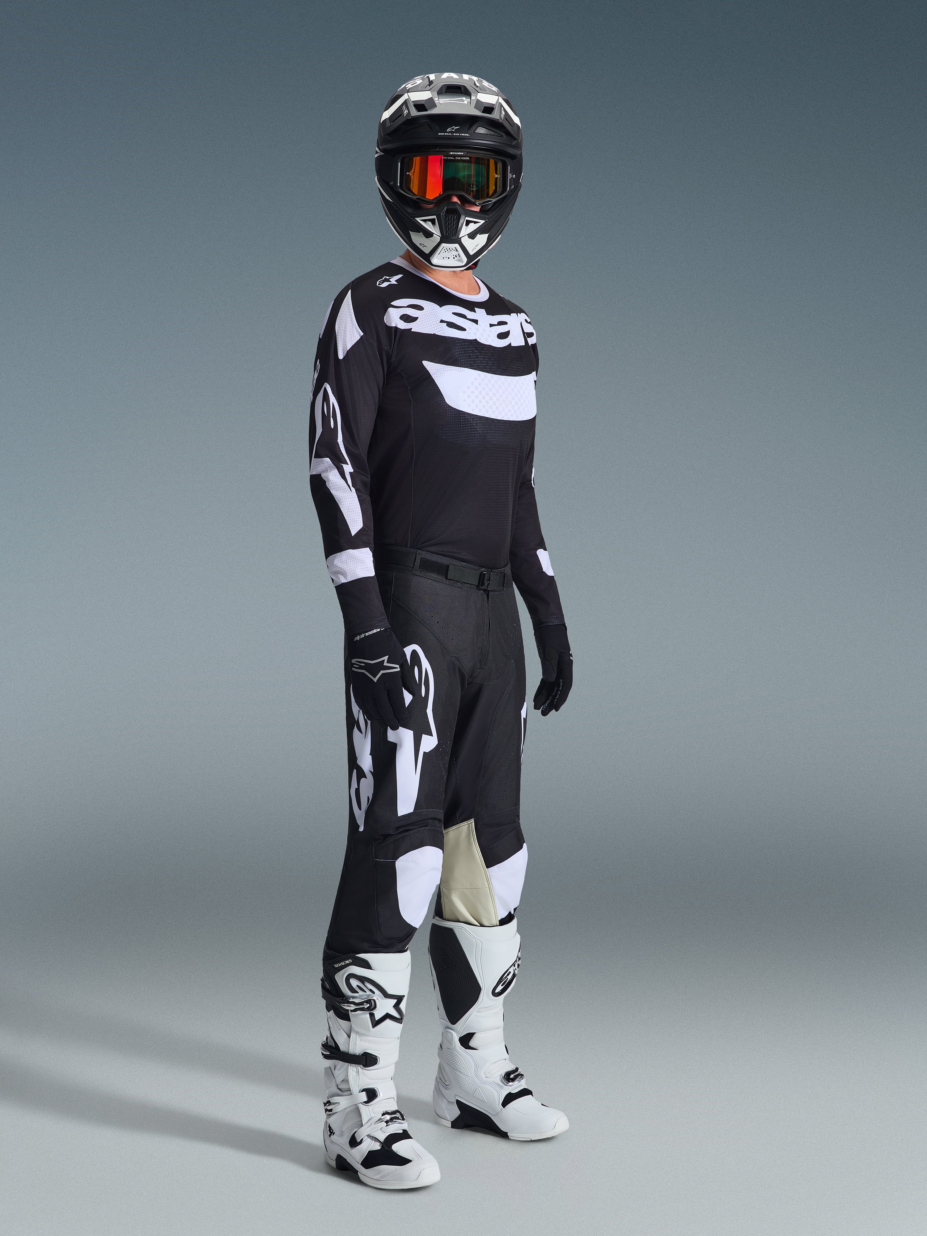 Alpinestars 2026 Racer Air Riway Gear Set, piloto de motocross con equipación completa de competición, jersey negro con marca 'Astars' en blanco y paneles de malla, pantalones negros con logotipos blancos grandes y paneles en las rodillas, casco negro con gafas rojas, botas blancas y negras, conjunto profesional de carreras todoterreno