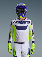 Motocross rider wearing the Alpinestars 2026 Racer Air Riway Gear Set, white mesh jersey with navy blue 'astars' branding and fluo yellow accents, matching white pants with navy and fluo yellow graphics, fluo yellow gloves, purple and fluo yellow helmet with white goggles, studio shot showing a complete off-road racing kit
