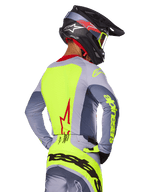 Jersey Alpinestars Techstar Melt 2025, Rojo Brillante Gris, vista trasera de un piloto de motocross con equipamiento de carreras gris y amarillo neón, logotipo de estrella roja en la espalda, casco negro y rojo a juego, indumentaria técnica para off-road