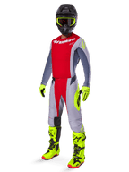 Piloto de motocross con el jersey Alpinestars 2025 Techstar Melt en rojo brillante y gris, con el pecho rojo y mangas grises con detalles en amarillo fluorescente. Combinado con pantalones a juego, botas y guantes de carreras en amarillo brillante, y un casco negro con gafas de montura amarilla para un equipo completo de carreras off-road.