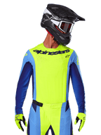 Alpinestars 2025 Techstar Melt Jersey, camiseta de motocross, amarillo flúor y azul, con ventilación cortada por láser y ajuste atlético de competición, usada por un piloto con casco negro y guantes amarillo flúor