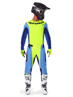 Piloto de motocross con equipamiento de competición completo, Jersey Alpinestars 2025 Techstar Melt en amarillo flúor y azul, pantalones de motocross a juego en amarillo y azul, casco negro con gráficos blancos y gafas, botas blancas y negras, guantes amarillos y negros, conjunto de alto rendimiento coordinado para carreras todoterreno