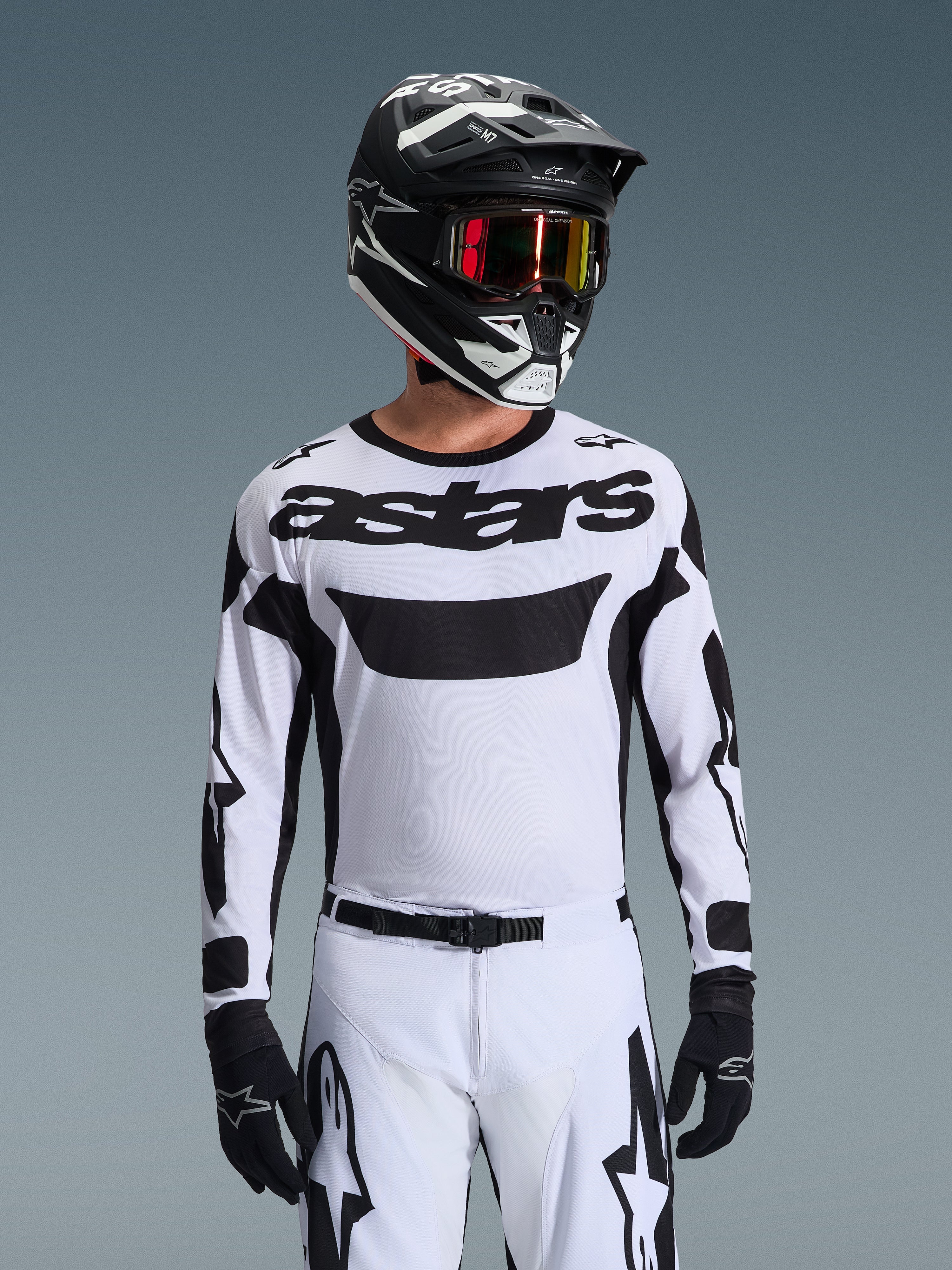 Piloto de motocross con el jersey Alpinestars Racer Riway 2026 en blanco y negro, con el logotipo 'astars' en el pecho, combinado con pantalones a juego en blanco y negro, casco negro con gafas y guantes negros, equipamiento coordinado para carreras off-road