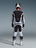 Piloto de motocross visto desde atrás con equipamiento completo de competición, Jersey Racer Riway 2026 en blanco y negro, pantalones a juego con la marca 'astars' en el asiento, casco negro con detalles blancos, guantes negros y botas blancas y negras, conjunto profesional coordinado de off-road